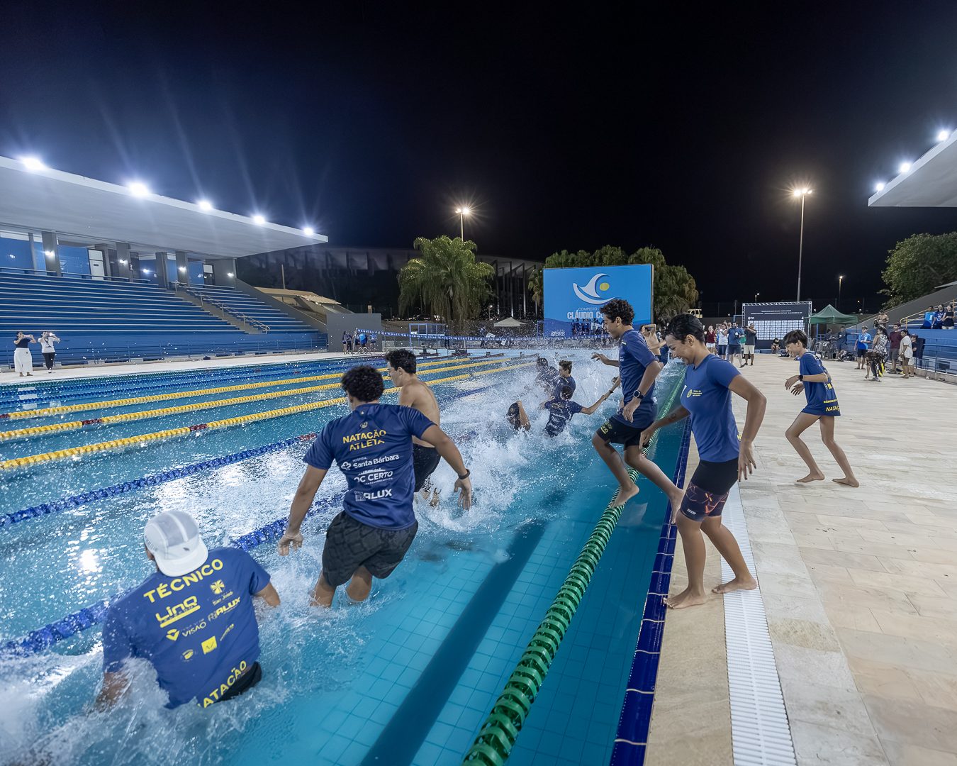 Atletas e comissões técnicas correm à beira da piscina, à noite, no fim da última etapa