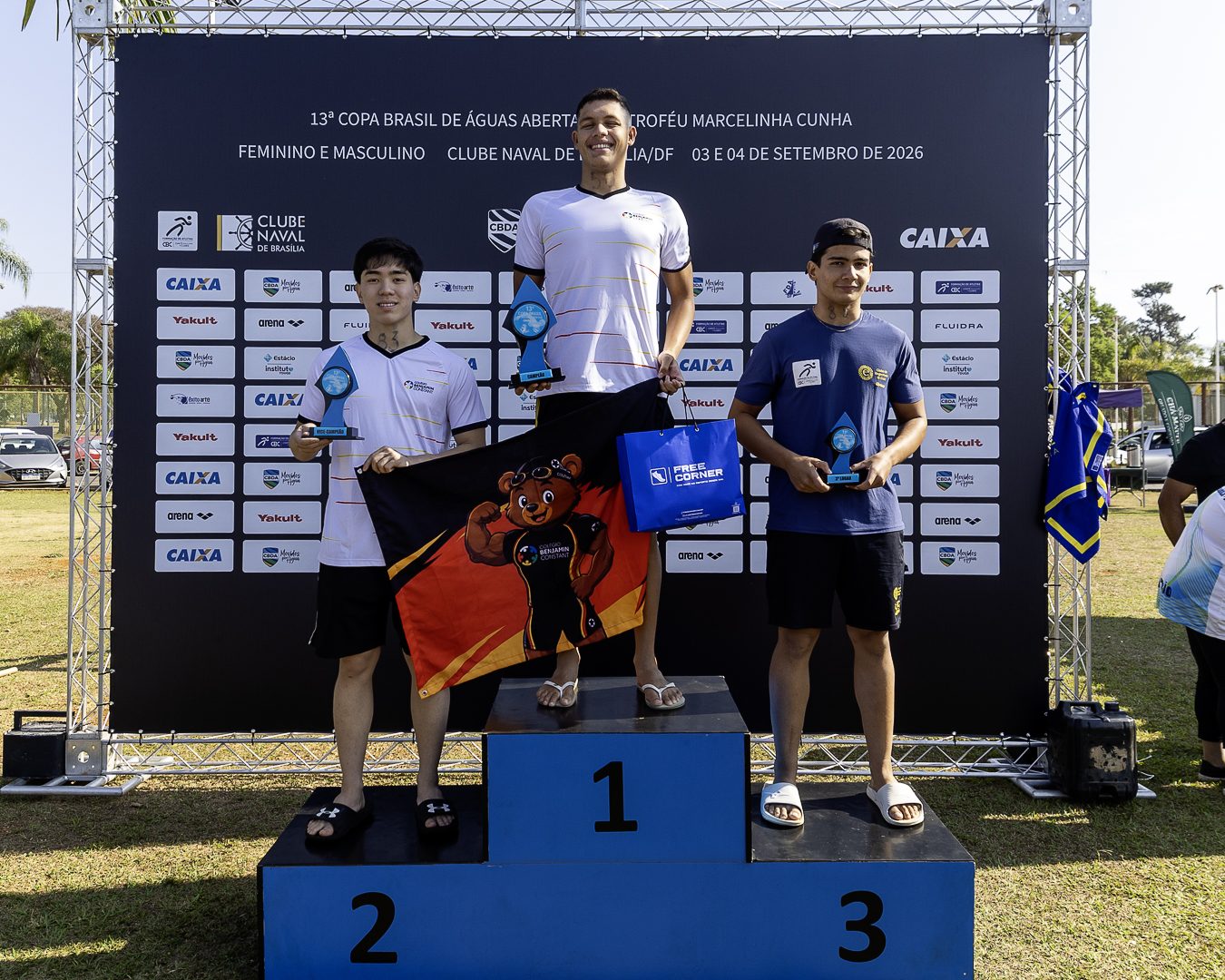 Pódio masculino no palco da Copa Brasil, com os três medalhistas segurando troféus diante do painel de patrocinadores
