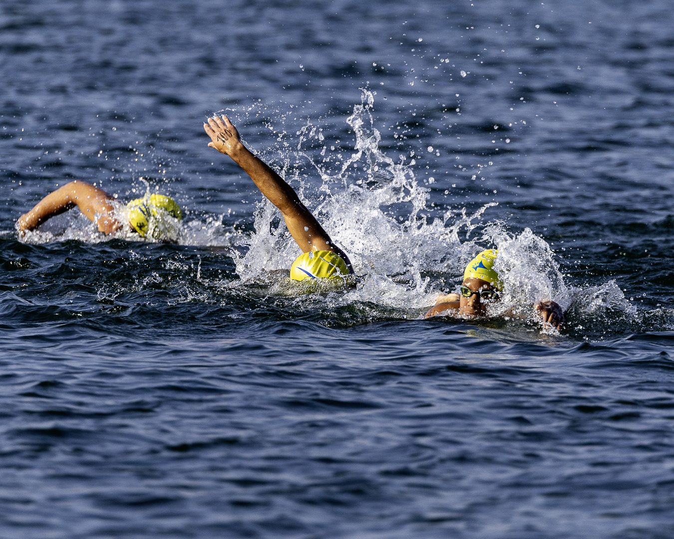 Três nadadores de touca amarela em nado crawl no Lago Paranoá