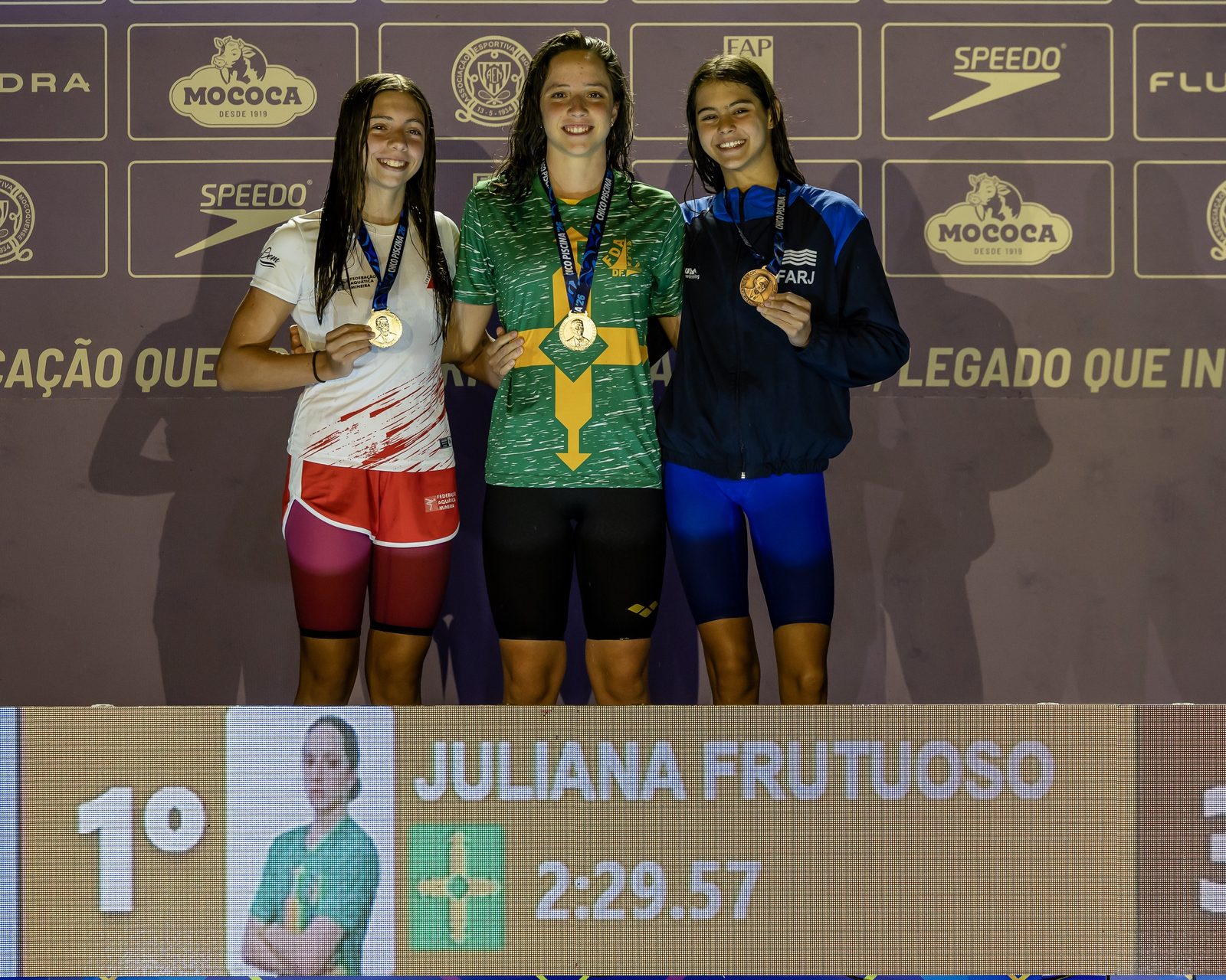 Pódio dos 200 metros medley infantil feminino: Juliana Frutuoso, do DF, com o ouro, entre a mineira Fernanda Tavares, prata, e a carioca Nina Figueiredo, bronze; no placar, o nome dela e o tempo de 2:29.57
