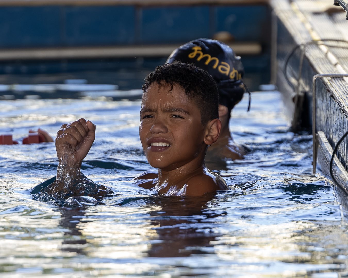 Atleta na água, junto à borda, cerra o punho em comemoração