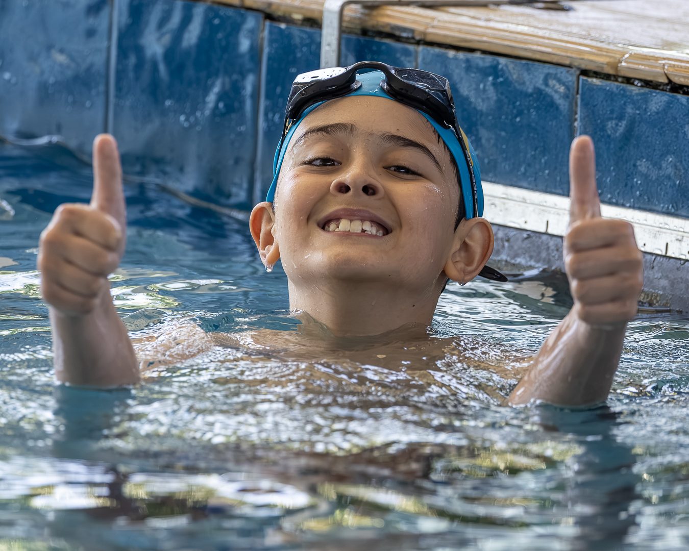 Atleta na água, junto à borda, sorri e faz sinal de positivo com as duas mãos