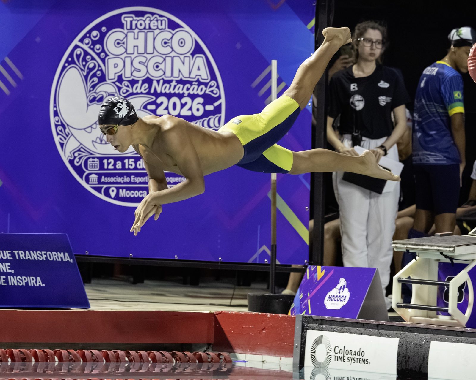 Atleta da Seleção do DF no ar, na saída, diante do painel do Troféu Chico Piscina 2026