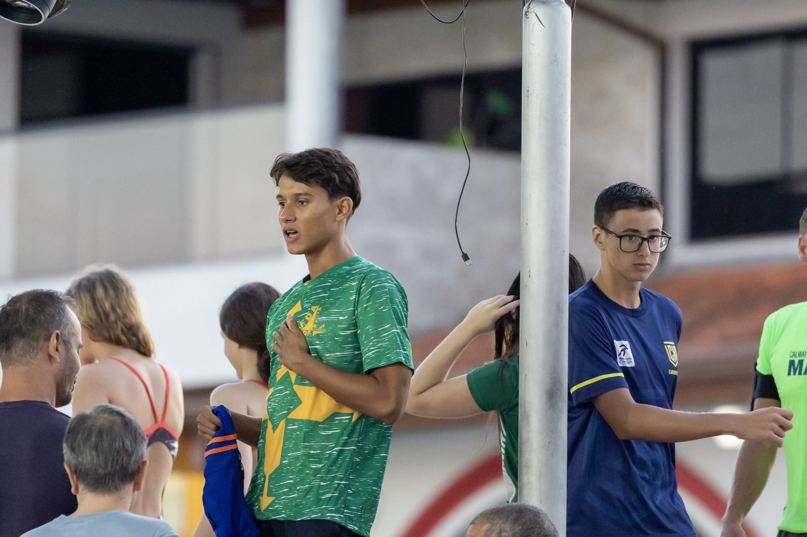 Atleta da Seleção do DF, de camisa verde e amarela, na beira da piscina entre outros atletas